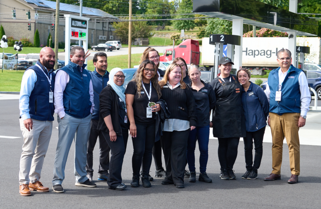 Group of diverse coworkers posing outdoors at a trucking facility, wearing staff badges. (informative)